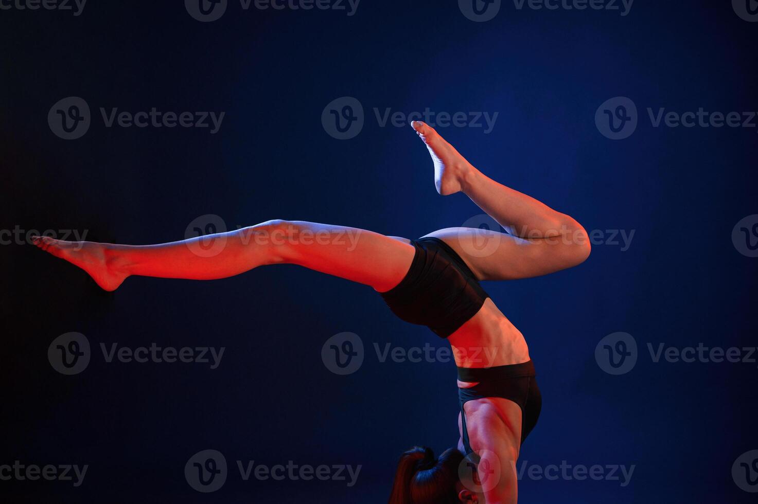 Doing ,hand, stand. Beautiful muscular woman is indoors in the studio with neon lighting photo