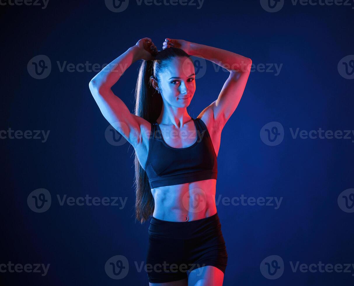 Fixes her hair. Beautiful ,muscular woman is indoors in the studio with neon lighting photo