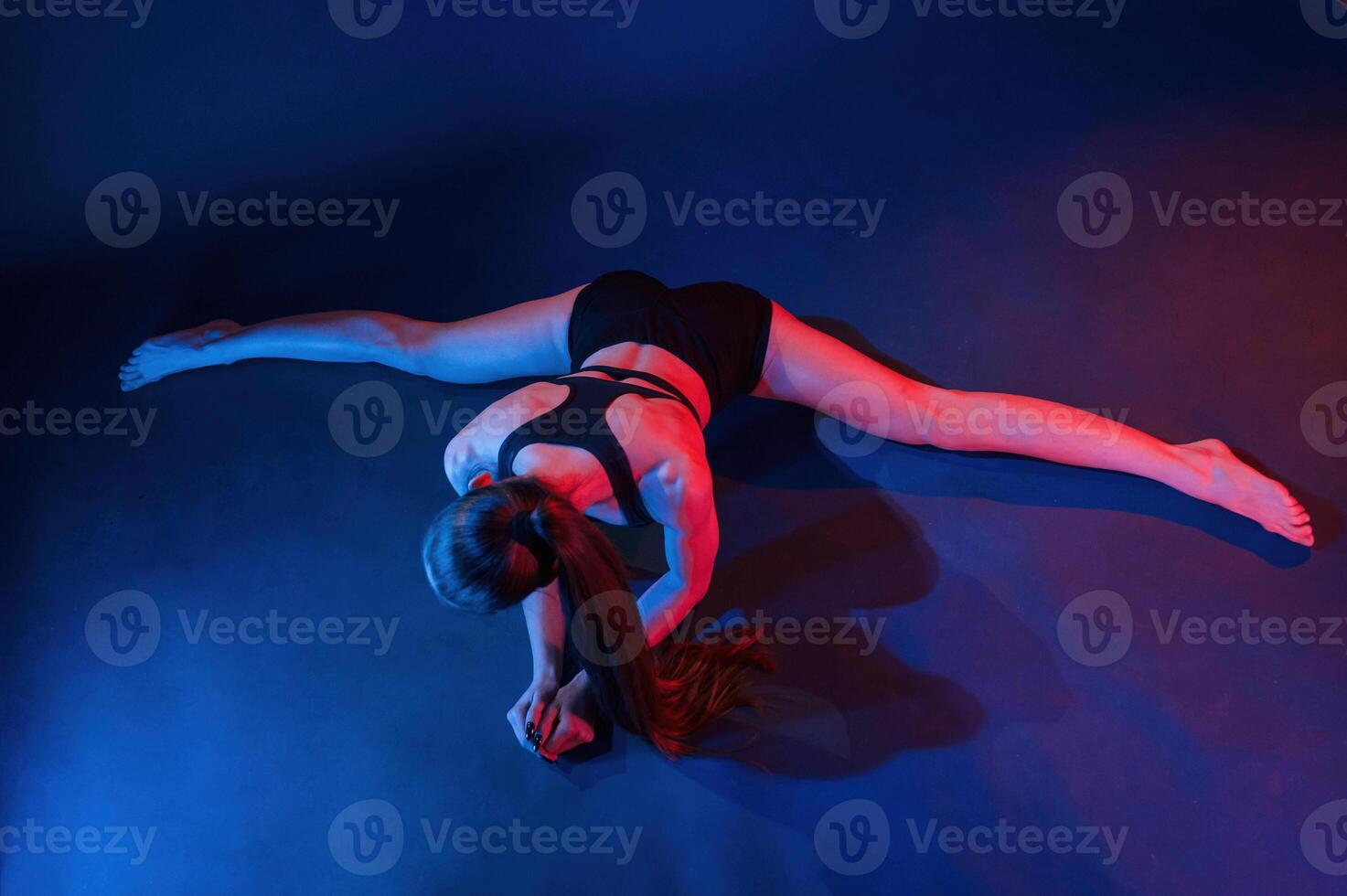 Performing the twine exercise. Beautiful, muscular woman is indoors in the studio with neon lighting photo