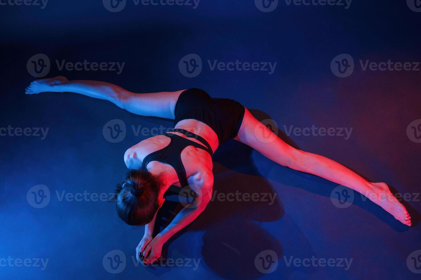 Performing the twine, exercise. Beautiful muscular woman is indoors in the studio with neon lighting photo