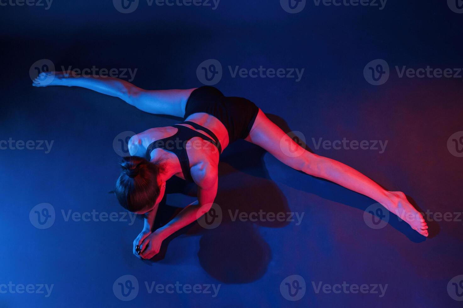 Performing the twine exercise. Beautiful muscular woman is indoors in the studio with neon lighting photo