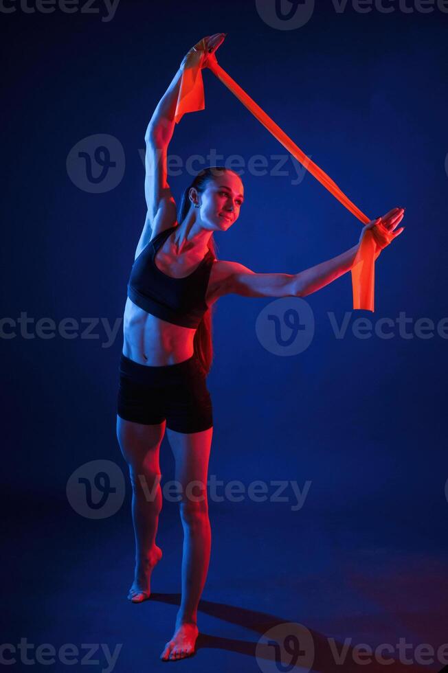 Holding, stretching ,tape in hands. Beautiful muscular woman is indoors in the studio with neon lighting photo