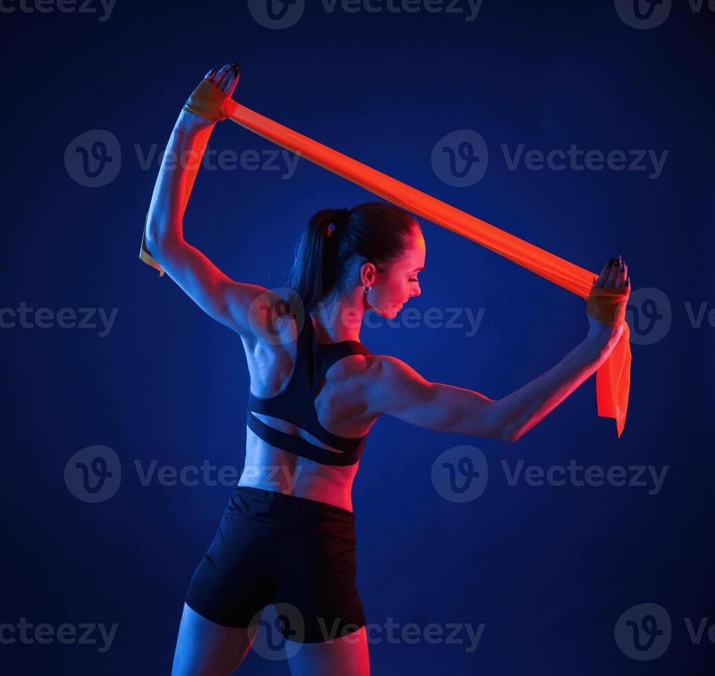 Yellow colored tape, for stretching the hands. Beautiful muscular woman is indoors in the studio with neon lighting photo
