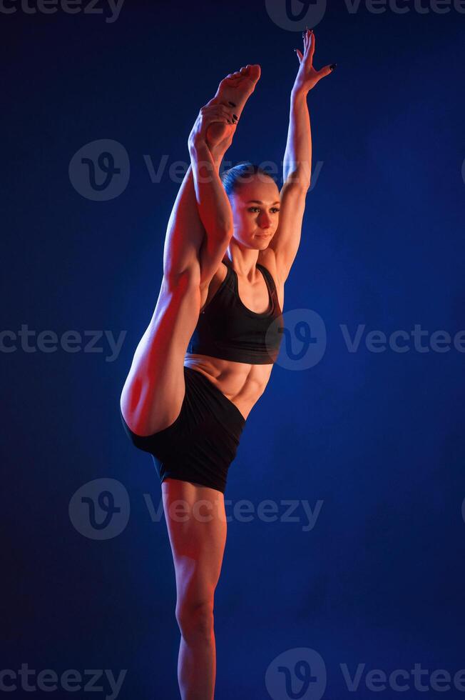 Leg stretching. Beautiful muscular woman is indoors in the studio with neon lighting photo