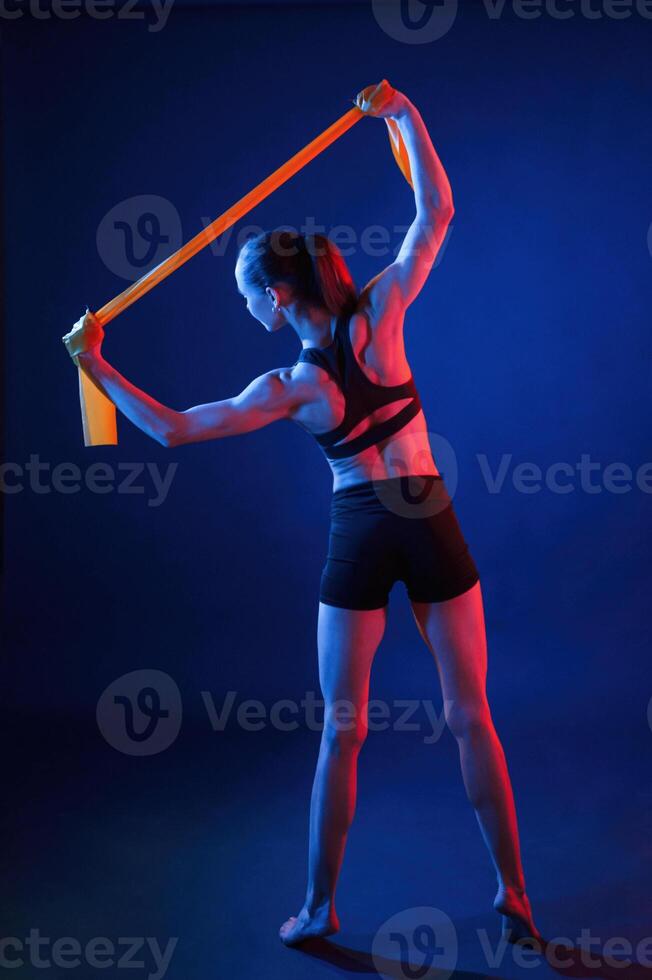 Yellow colored tape for stretching the hands.. Beautiful muscular woman is indoors in the studio with neon lighting photo