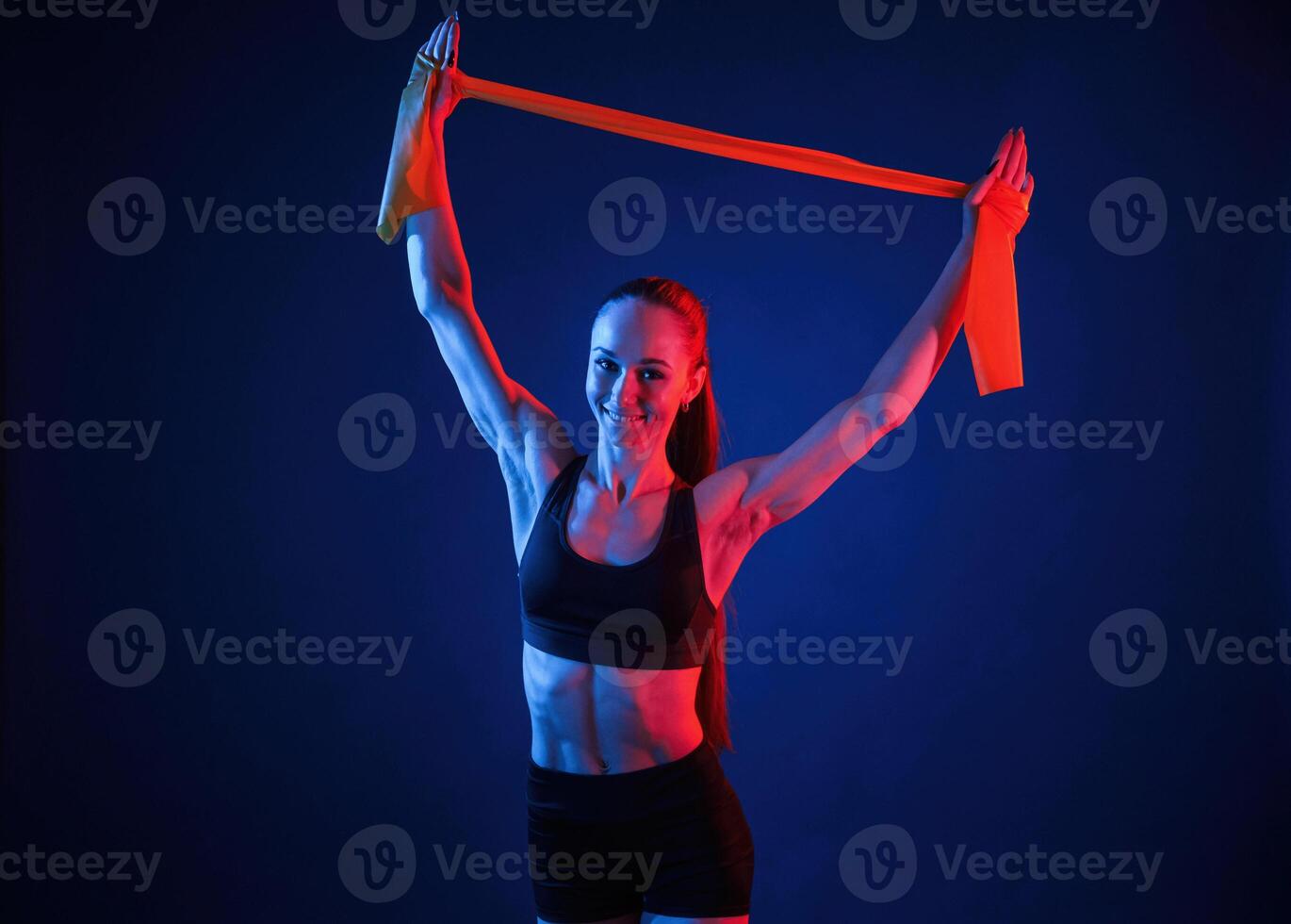 Yellow colored tape ,for stretching the hands. Beautiful muscular woman is indoors in the studio with neon lighting photo