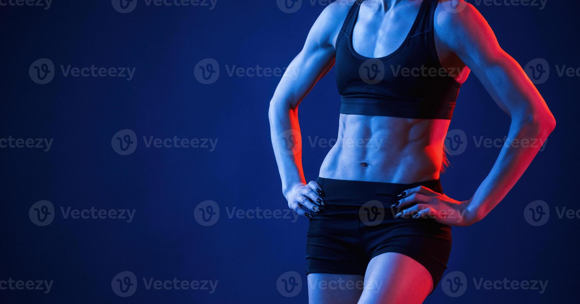 Close up view of abs.. Beautiful muscular woman is indoors in the studio with neon lighting photo
