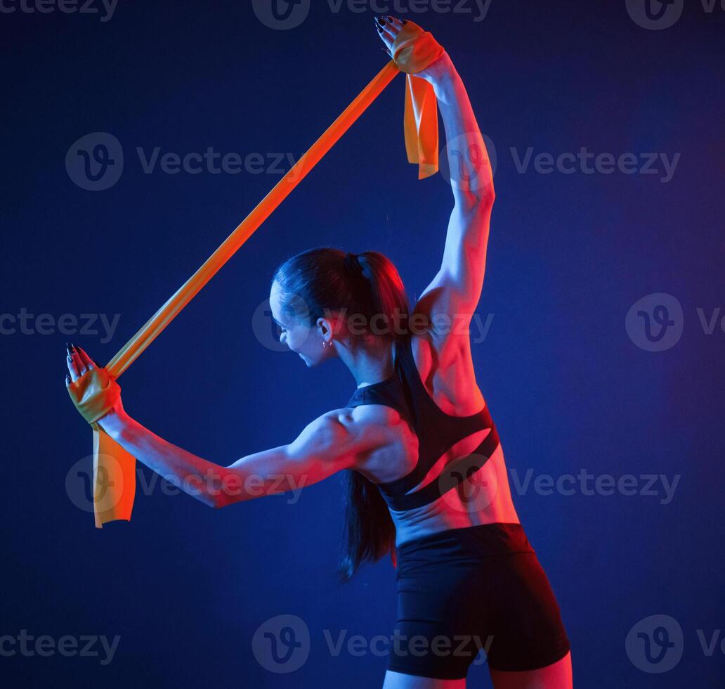Holding stretching, tape in hands. Beautiful muscular woman is indoors in the studio with neon lighting photo