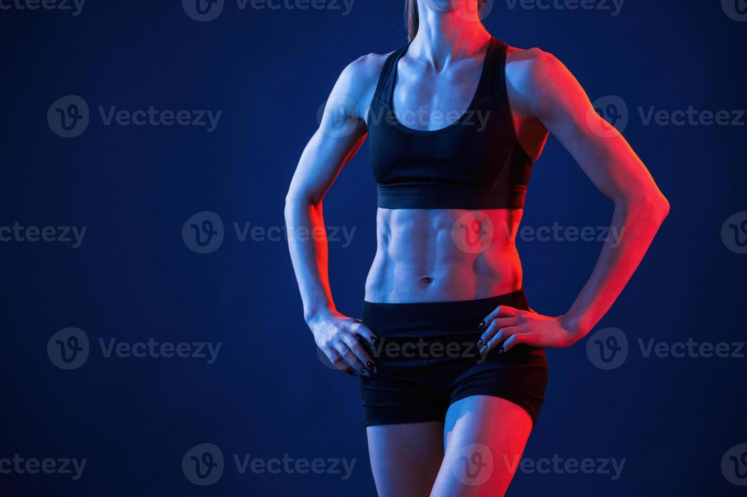 Close up view of abs. Beautiful muscular woman is indoors in the studio with neon lighting photo