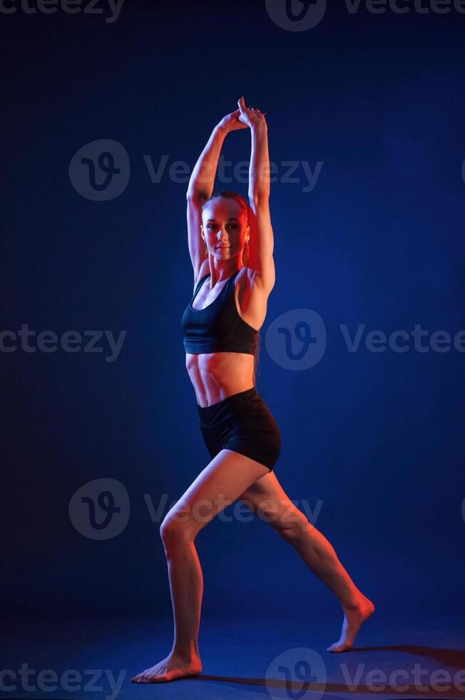 Sportive ,exercises, standing, and stretching the hands. Beautiful muscular woman is indoors in the studio with neon lighting photo
