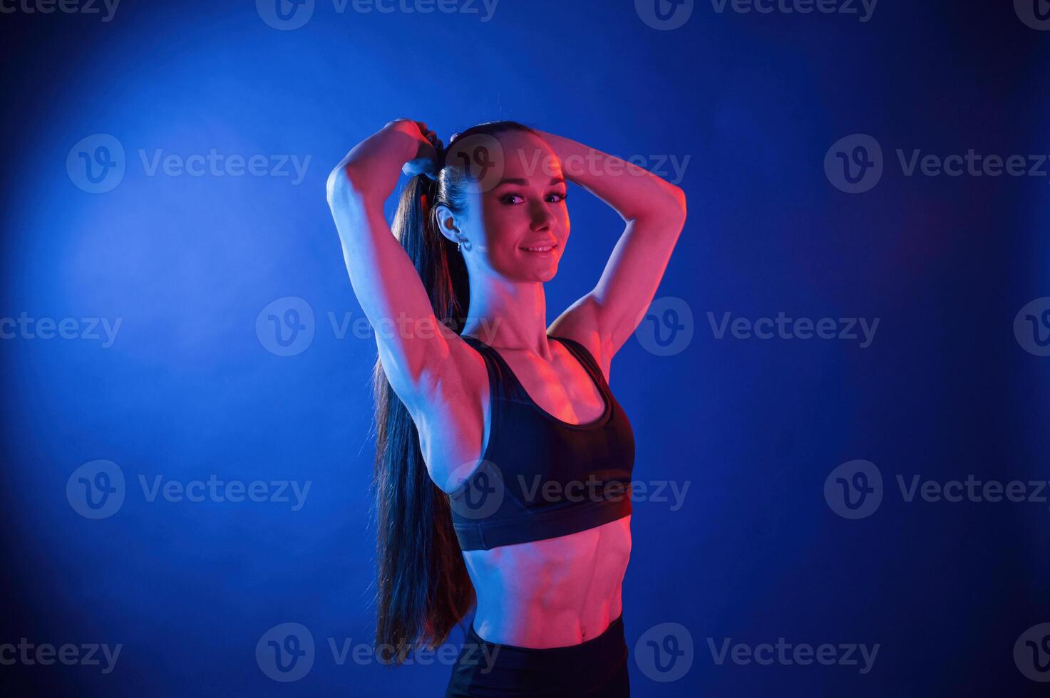 Fixes ,her hair. Beautiful muscular woman is indoors in the studio with neon lighting photo