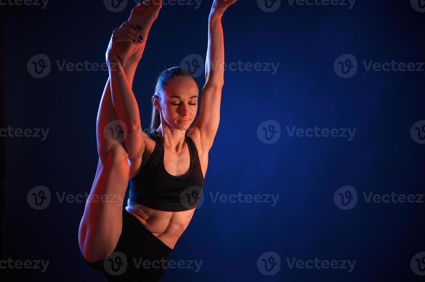 Raising, up the leg, exercise. Beautiful muscular woman is indoors in the studio with neon lighting photo