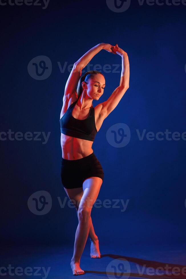 Sportive e,xercises, standing, and stretching the hands. Beautiful muscular woman is indoors in the studio with neon lighting photo