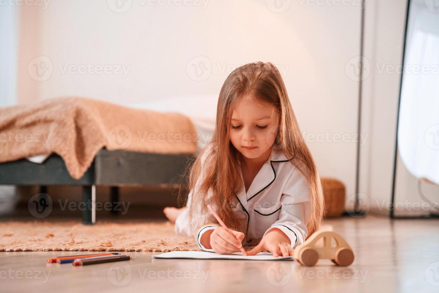 Little girl is lying down on the floor at home and drawing photo