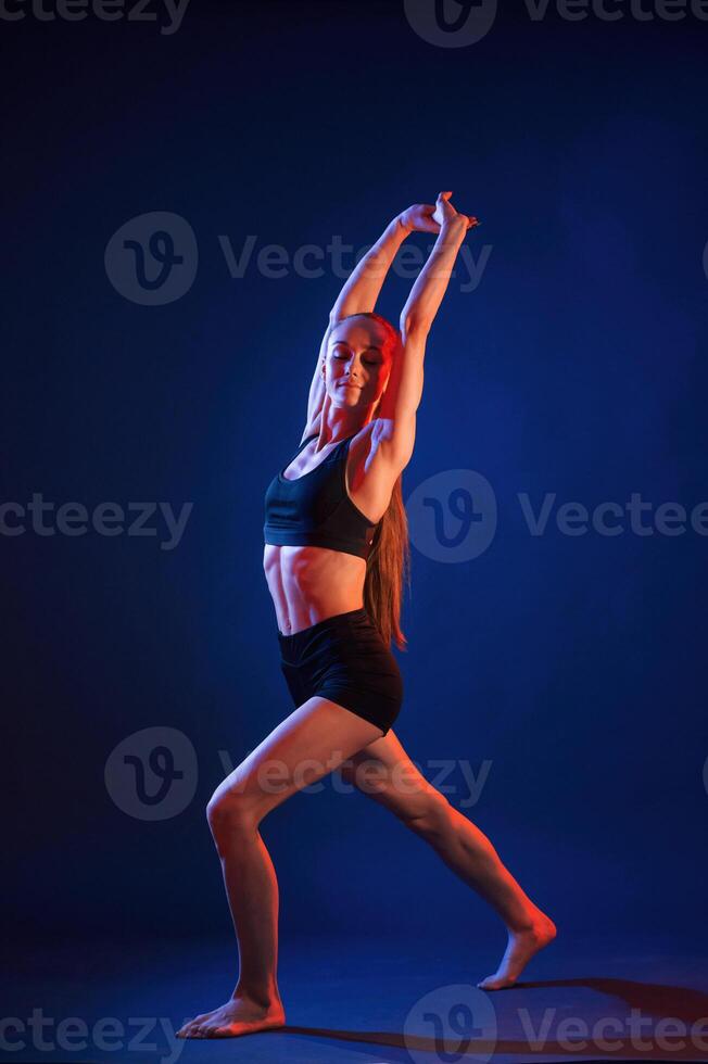 Sportive ,exercises, standing and stretching the hands. Beautiful muscular woman is indoors in the studio with neon lighting photo
