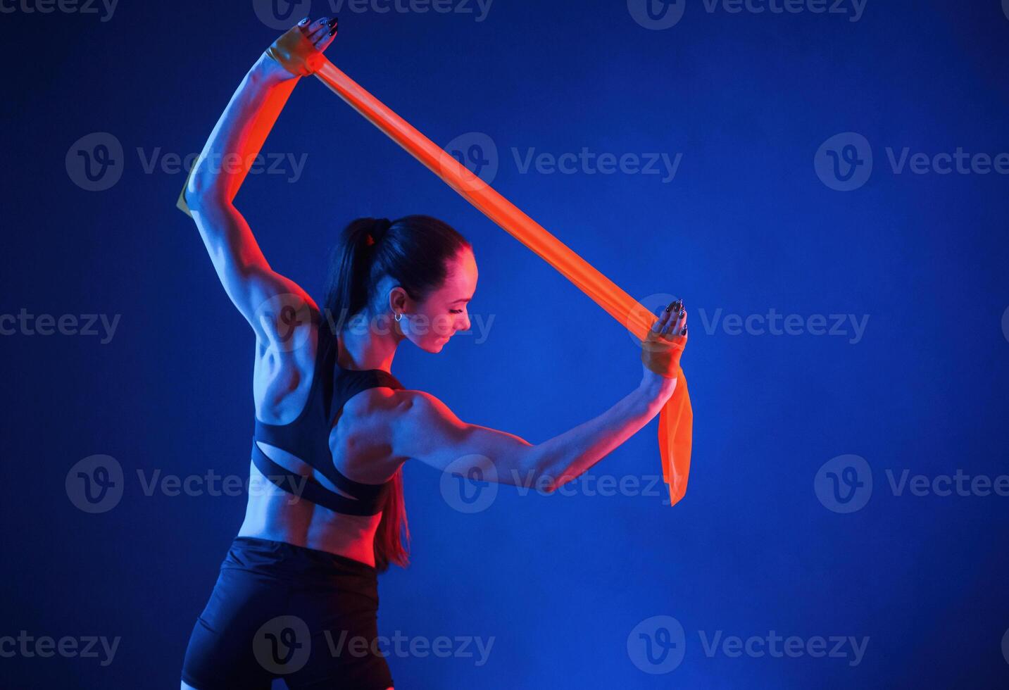 Holding ,stretching tape in hands. Beautiful muscular woman is indoors in the studio with neon lighting photo