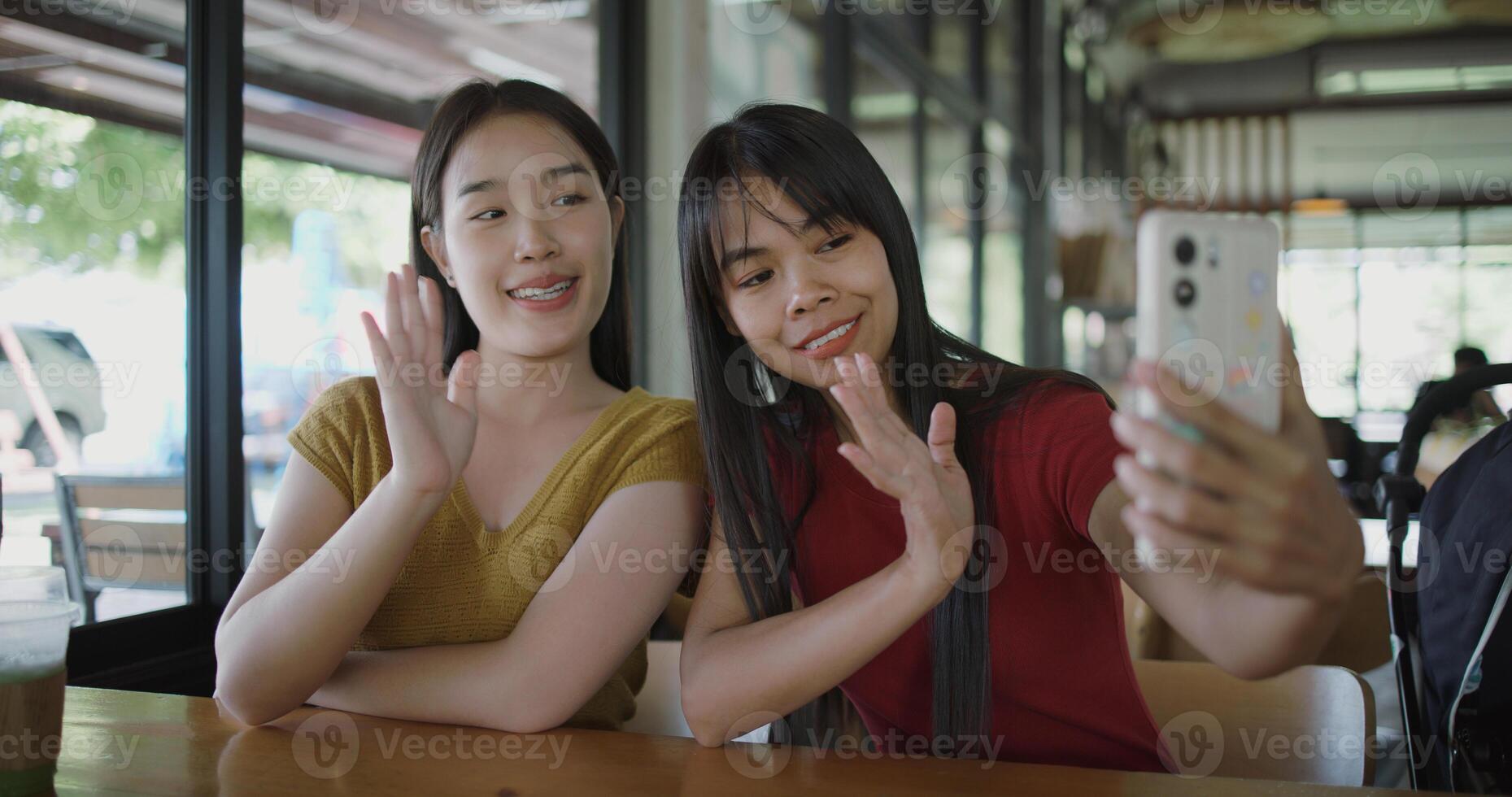 Portrait of Two Asian women are enjoying talking with a friend via call on mobile phone at a table in a coffee shop. Family enjoying time together. Happy lifestyle. photo