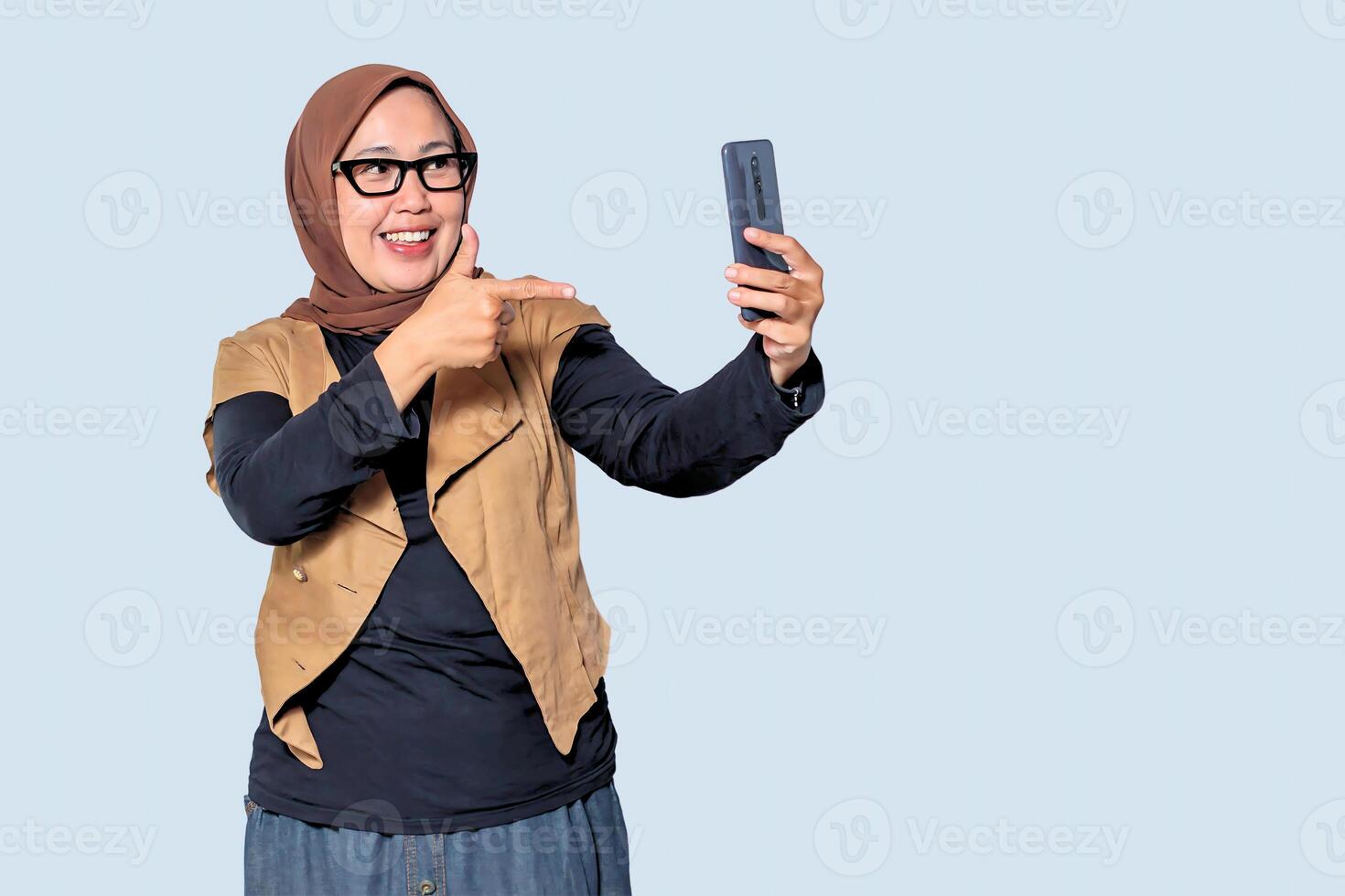 A happy Muslim woman in a hijab taking a selfie with her smartphone, expressing joy and confidence in a modern digital lifestyle photo