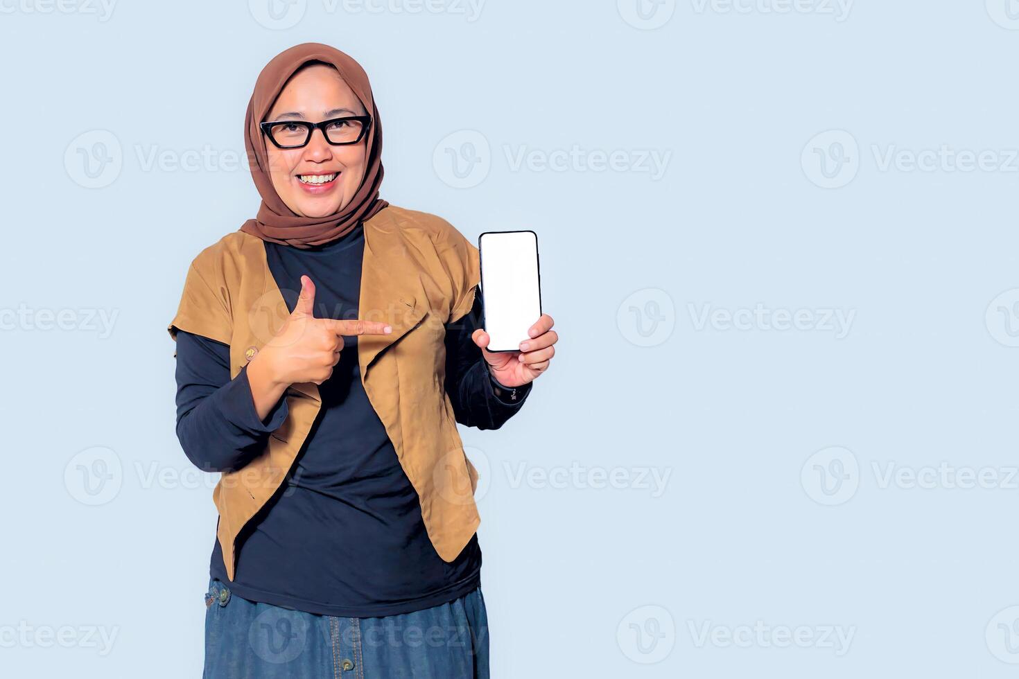 A confident Muslim woman in hijab presenting a smartphone with a blank screen photo