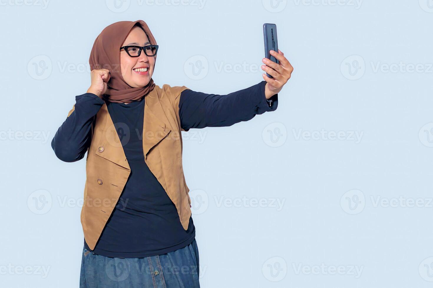 A happy Muslim woman in hijab taking a selfie with a smartphone, smiling with joy photo