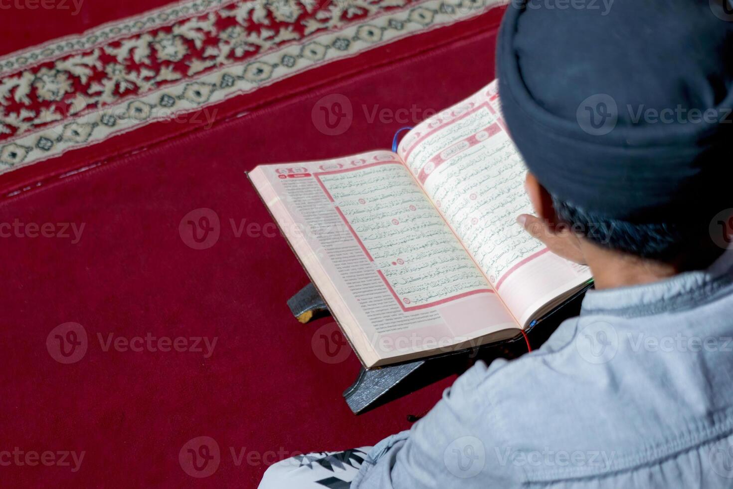 Man Reading the Quran on a Red Carpet in a Peaceful Setting photo