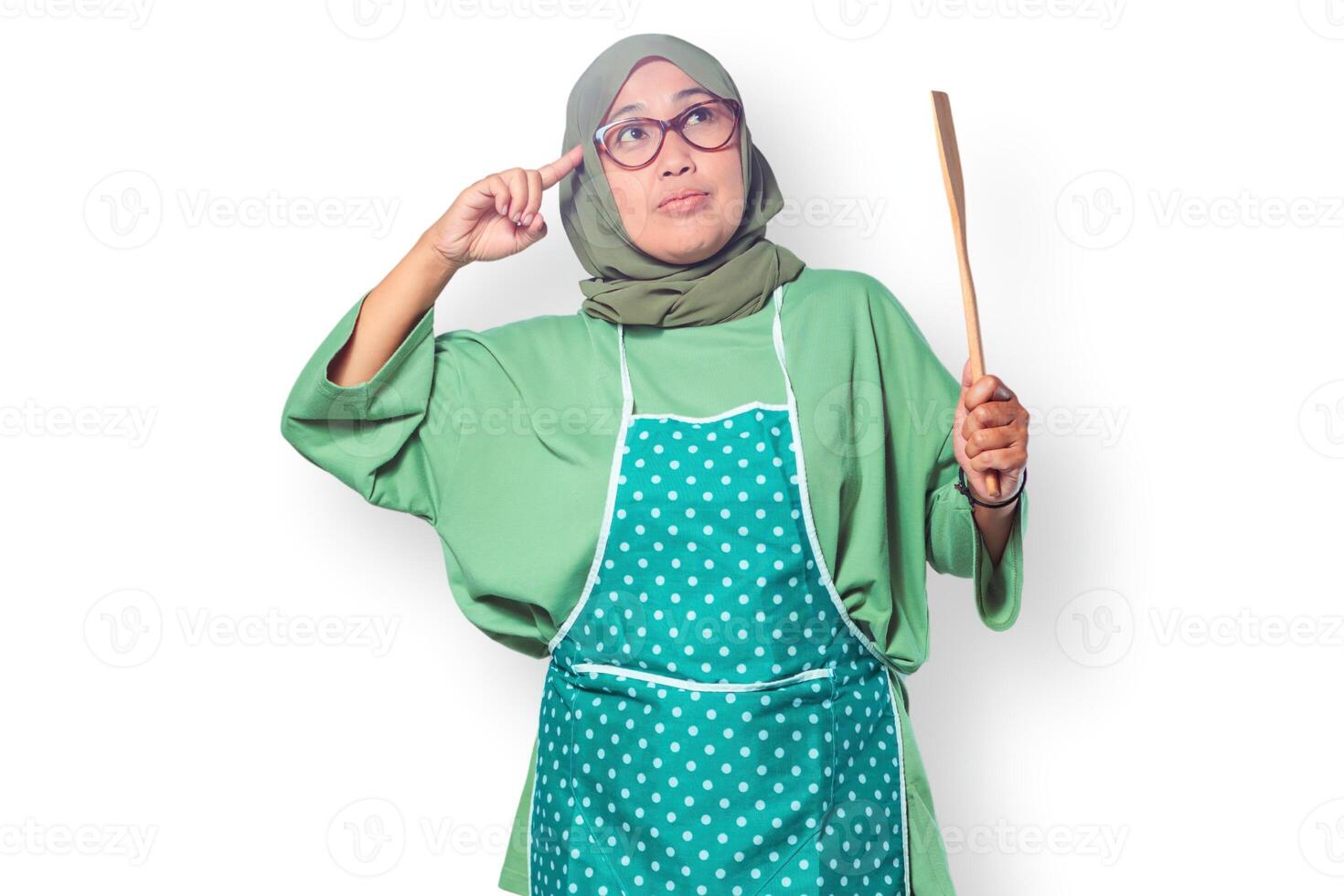 Muslim woman in a hijab and apron holding a wooden spatula, thinking about cooking ideas photo