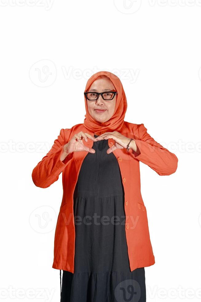 Confident Muslim woman in an orange hijab showing a heart gesture, symbolizing positivity and empowerment in a modern setting photo