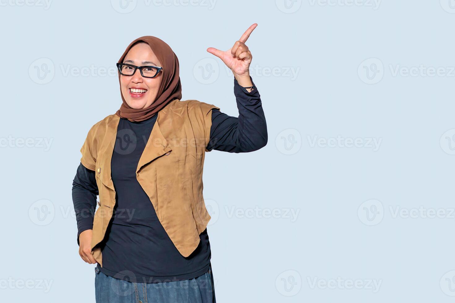 A confident Muslim woman in a hijab pointing up with a happy and energetic expression photo