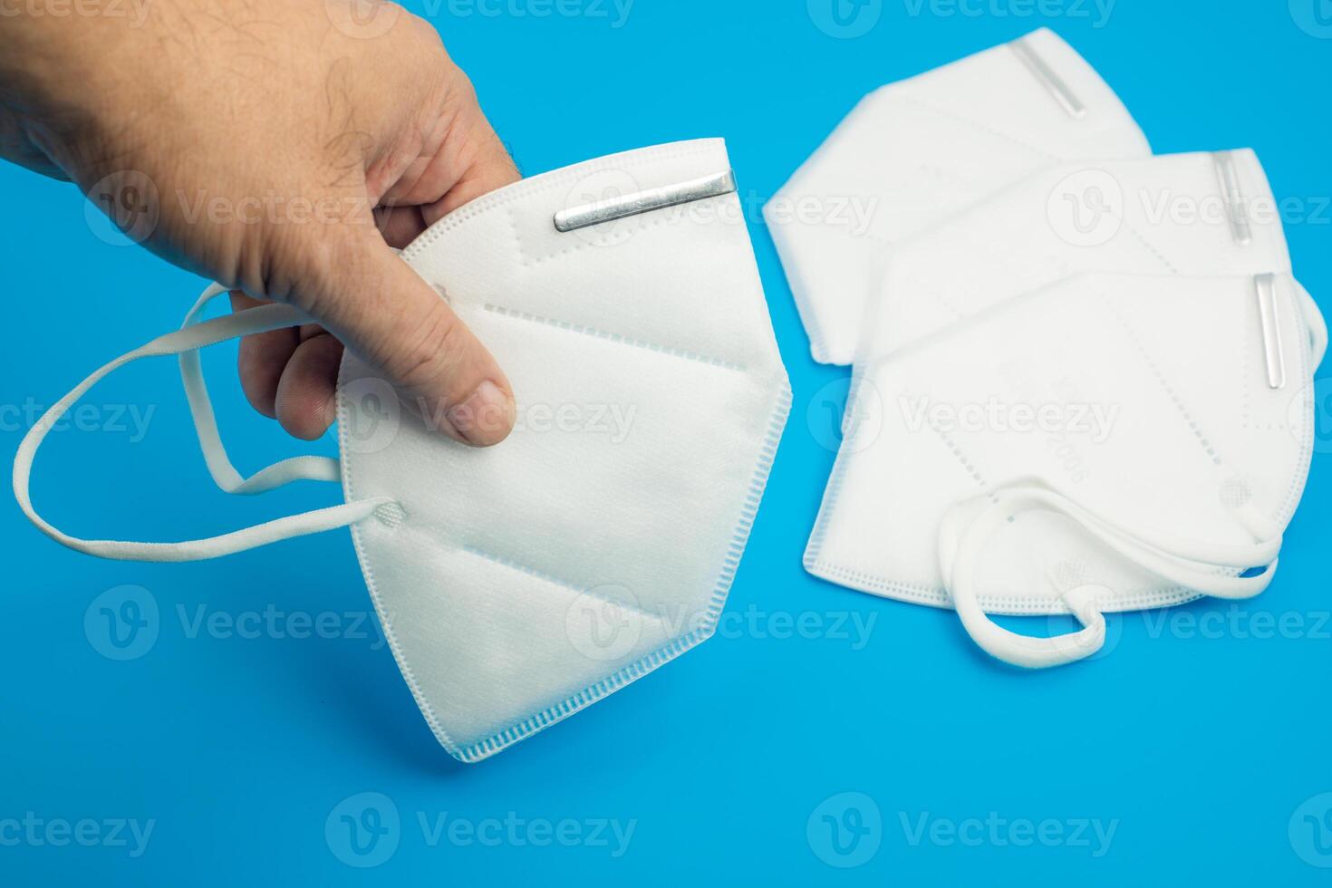 Hand holding a white face mask near additional masks on a blue background photo