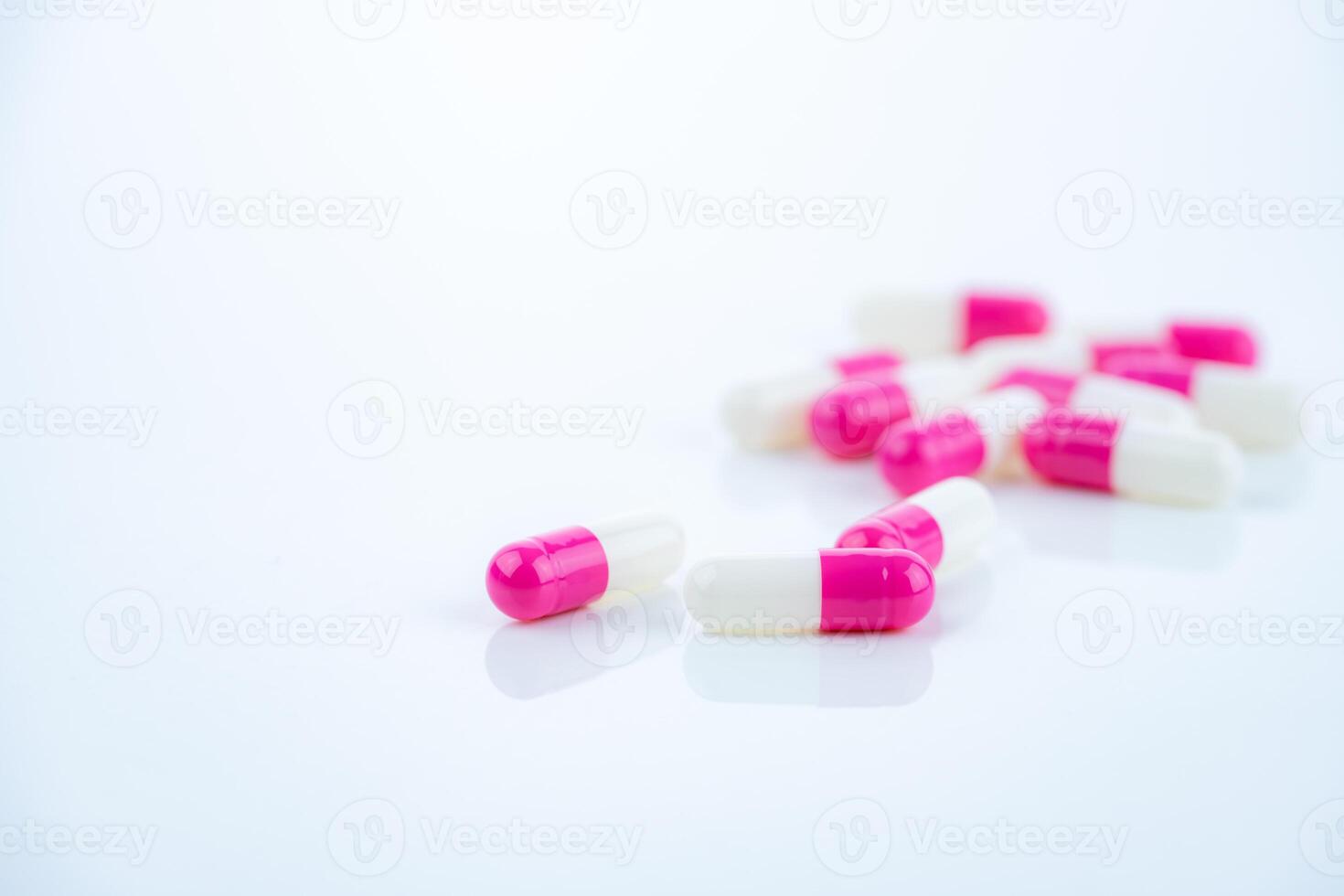 Pink-white antibiotic capsules spread on white background. Prescription drug. Antibiotic resistance in modern medicine. Healthcare and pharmaceutical industry. Medical care, pharmaceutical research photo