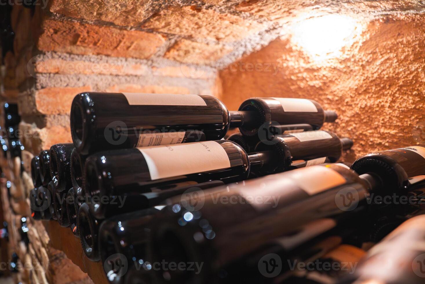 A wine cellar with bottles neatly stacked on their sides, rustic brick and stone walls, and soft lighting highlighting the organized display. photo