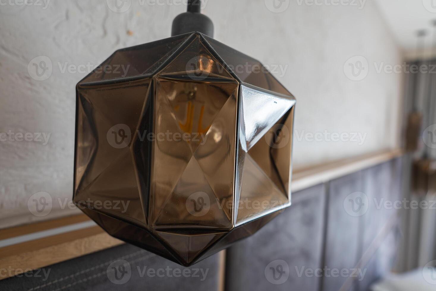 Close up of a metallic, angular pendant light with a smoky finish, set against a textured wall and upholstered panels in a luxury hotel in Ischgl, Austria. photo
