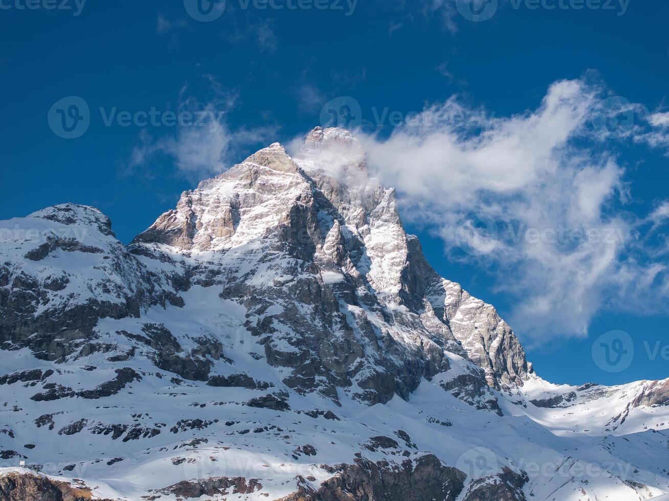 The iconic Matterhorn mountain in the Alps features a pyramid like peak, rugged rock formations, and snow covered slopes under a clear blue sky. photo