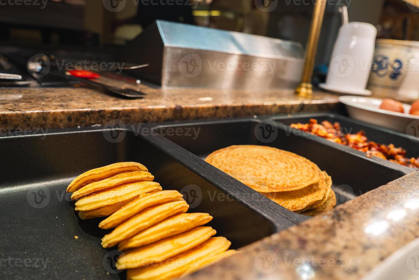Neatly arranged pancakes on black trays with bacon and utensils on a granite countertop in a high end hotel dining area in Ischgl, Austria. photo