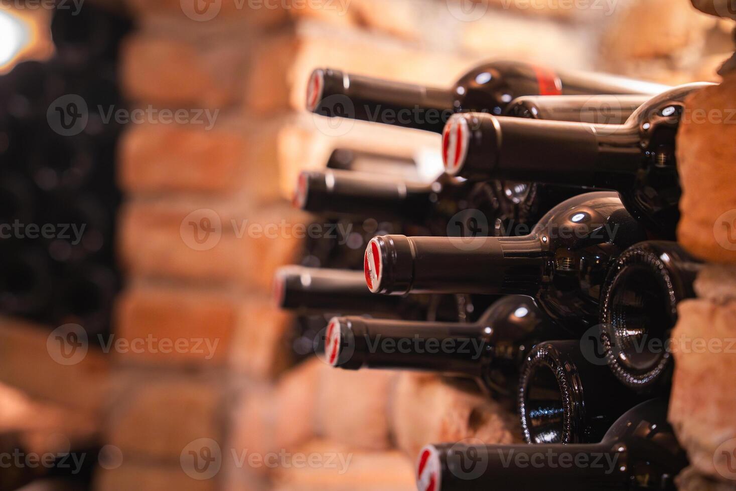 Neatly arranged wine bottles stored horizontally in a brick wall wine rack, with warm lighting highlighting the bricks and glossy bottle surfaces. photo