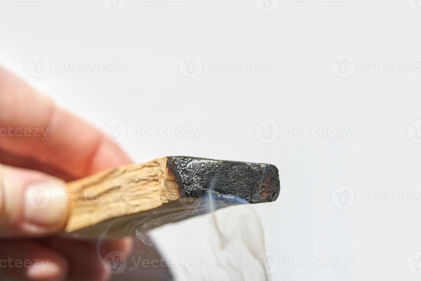 Hand holding smoldering palo santo stick with rising smoke against white background. photo
