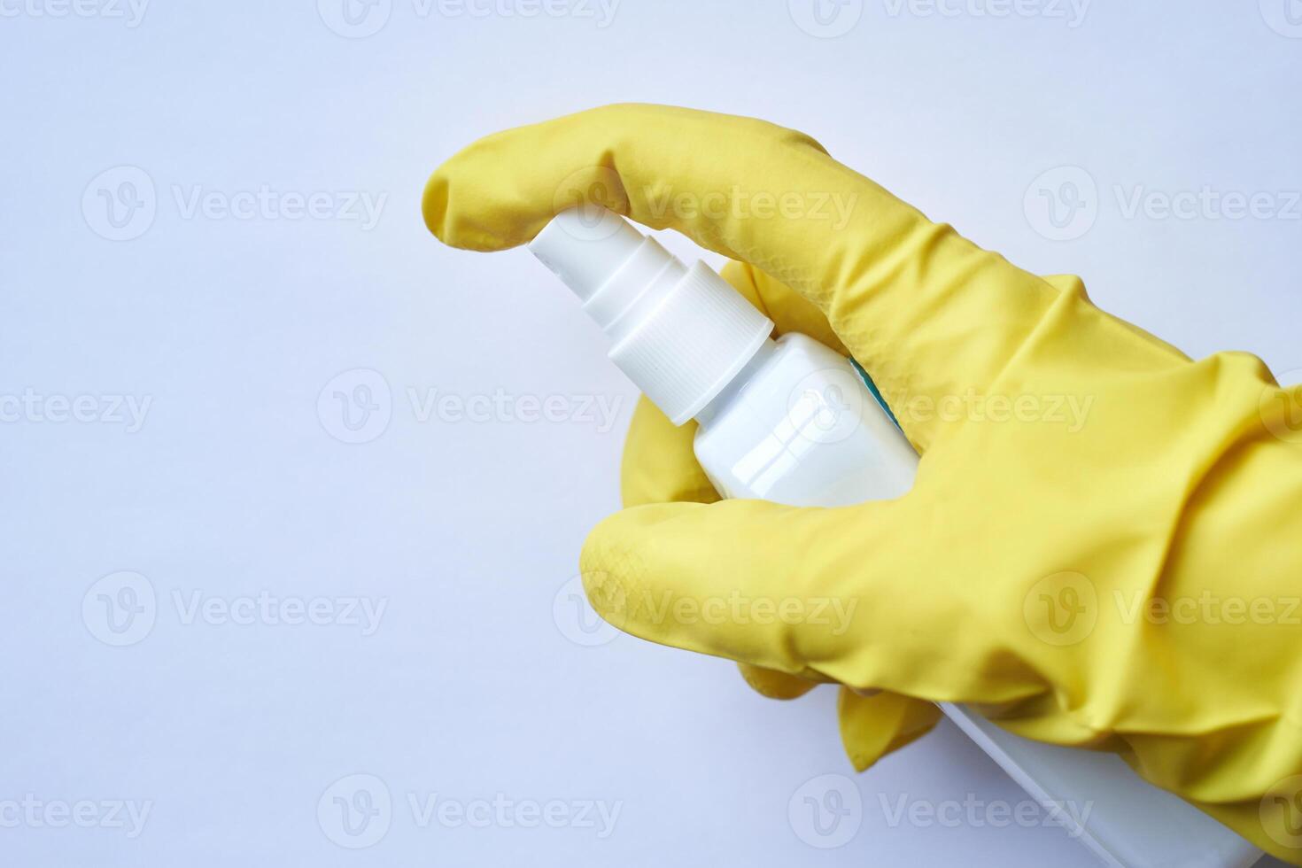 Hand in yellow glove holding white spray bottle against light background for cleaning or sanitizing use. photo