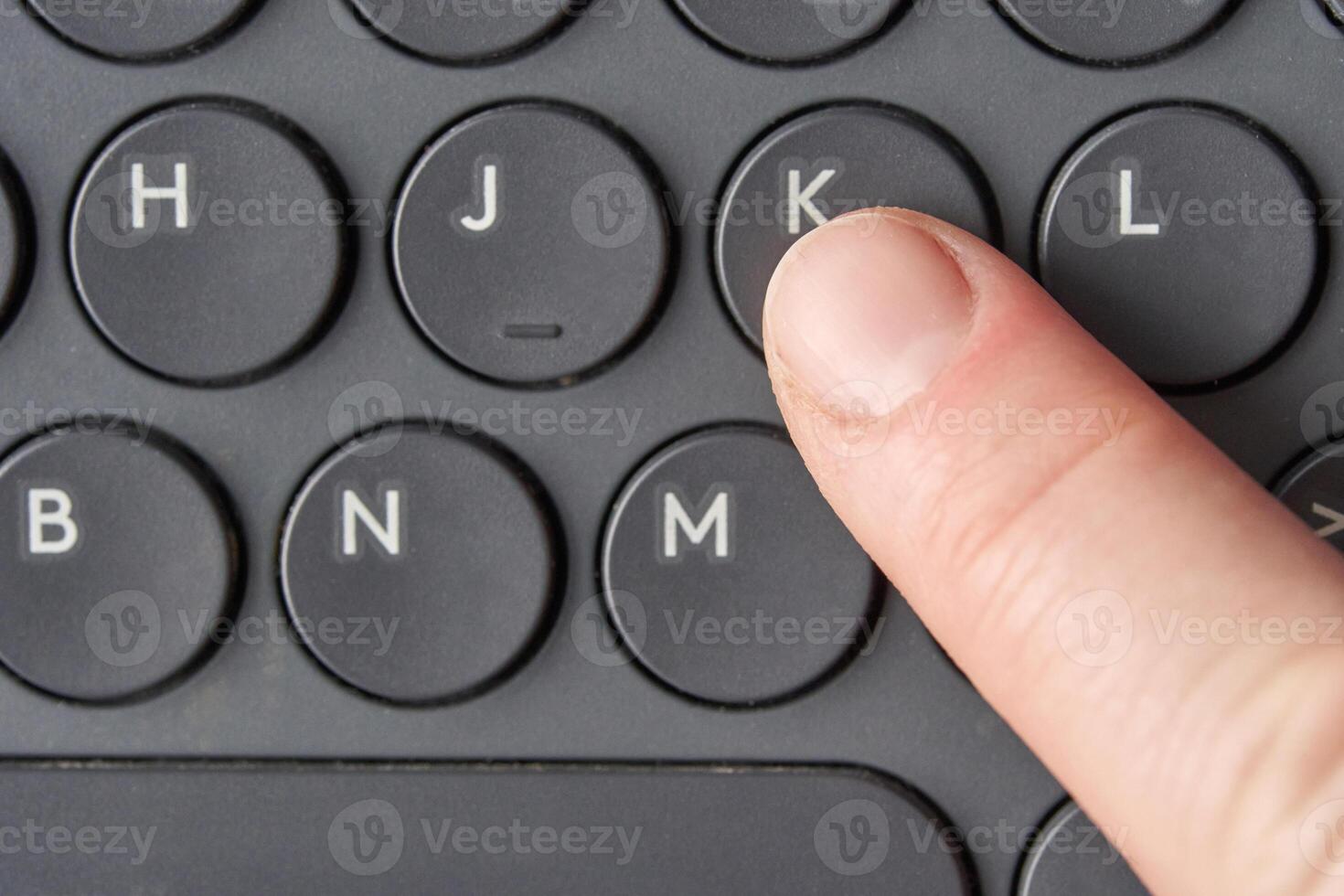 Close up of finger pressing k key on black keyboard with circular buttons. photo