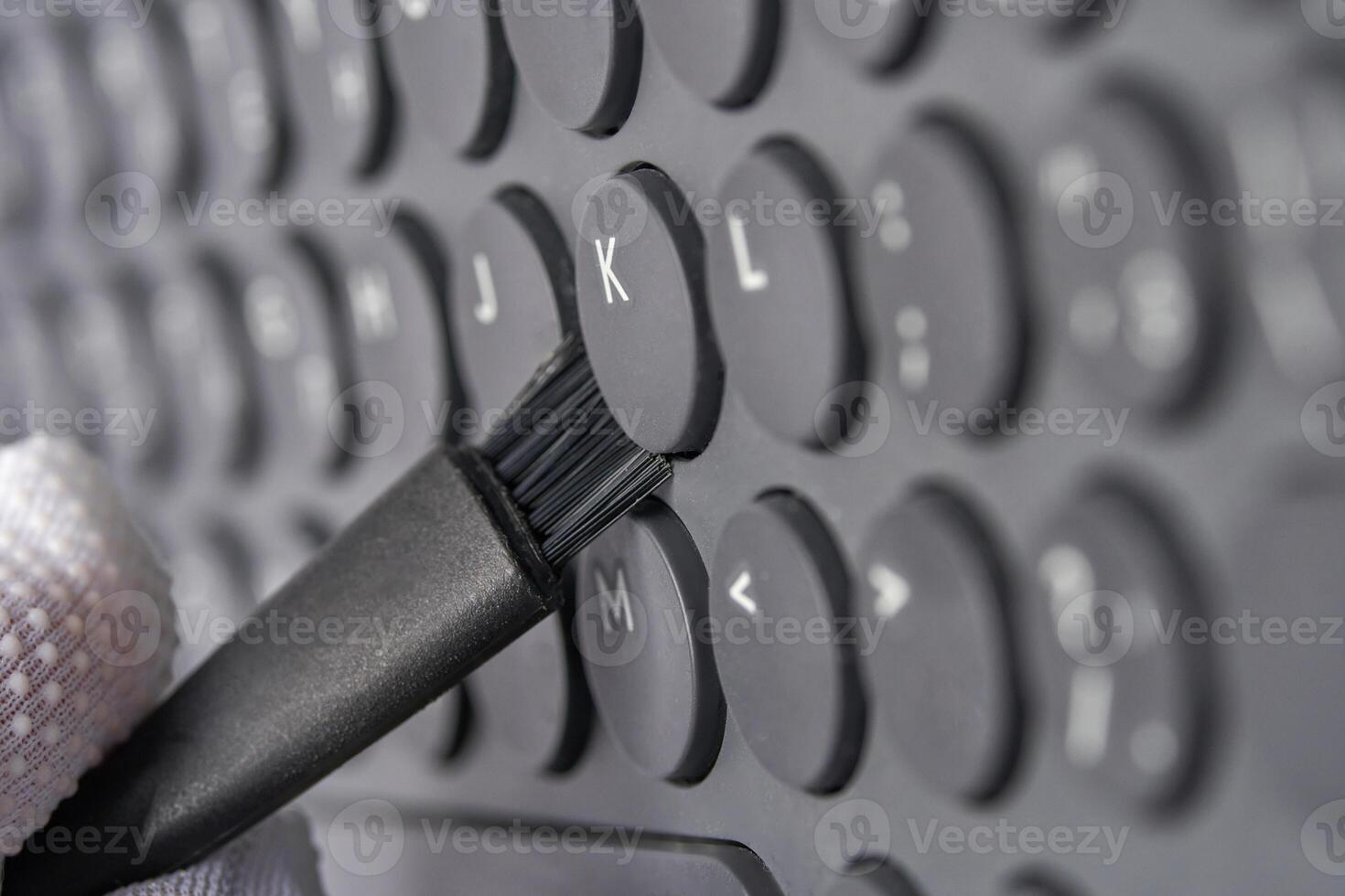 Close up of gloved hand cleaning keyboard with small brush for maintenance and hygiene. photo