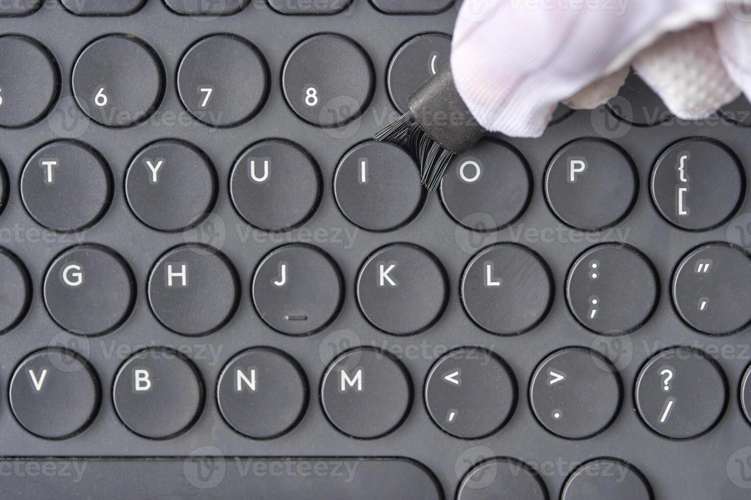 Gloved hand cleaning black computer keyboard with brush close up technology hygiene concept. photo