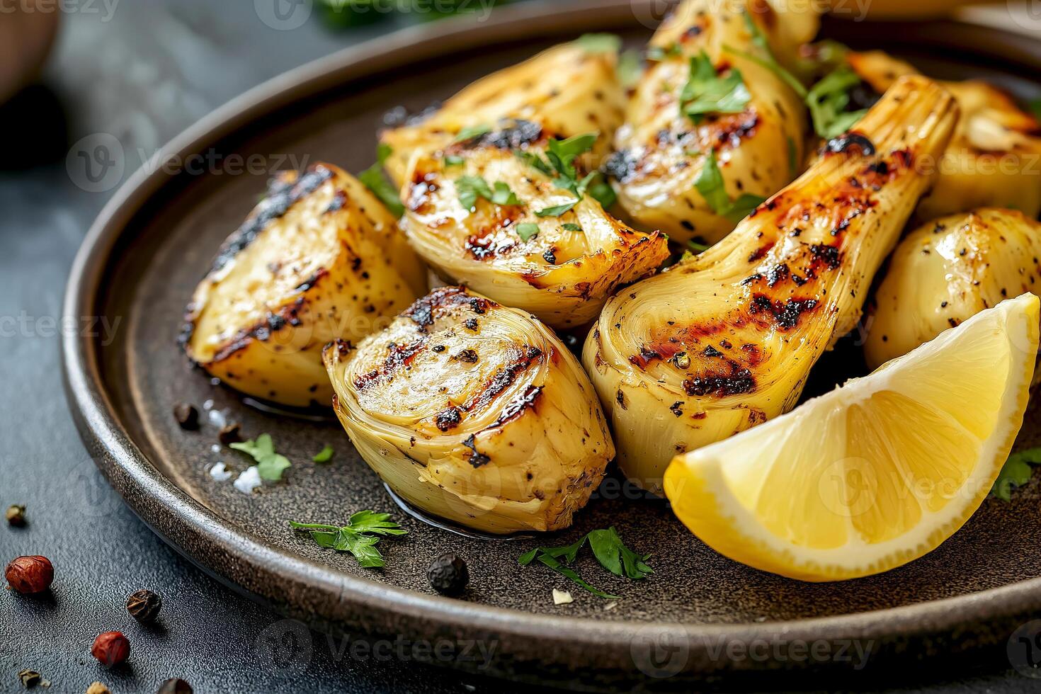 Grilled artichoke hearts with lemon wedge and herbs on dark plate served at a rustic table setting. Roasted artichoke hearts garnished with fresh herbs and accompanied by a lemon wedge, healthy snack photo