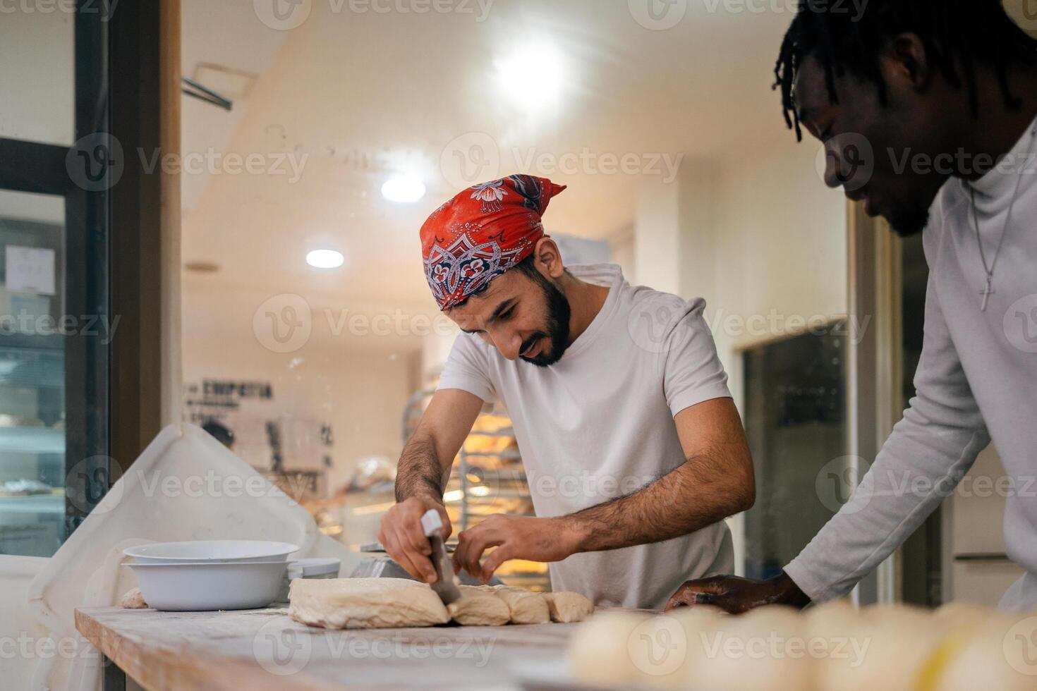 Two men in white shirts and red bandanas are making bread photo