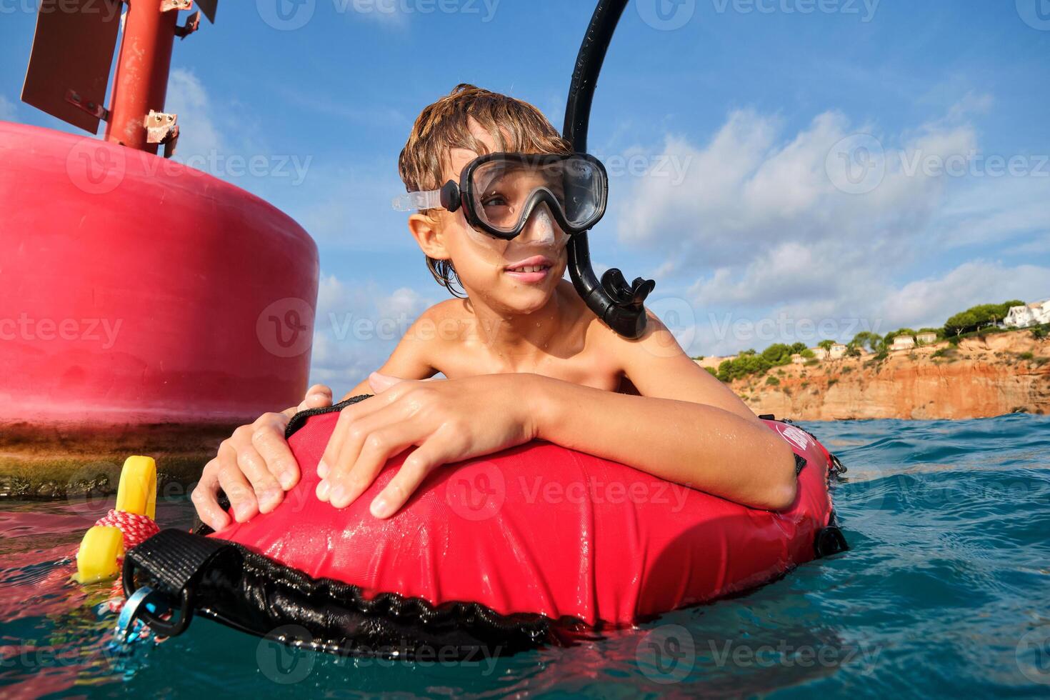 Happy kid in diving mask in seawater near red buoy. photo