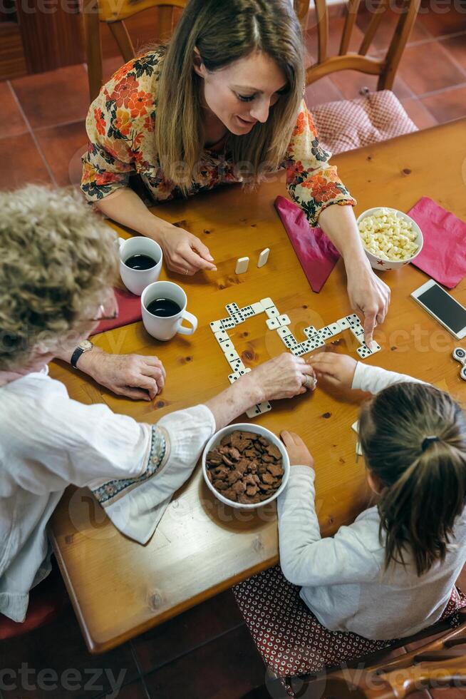 A woman and two children playing dominoes at a table photo