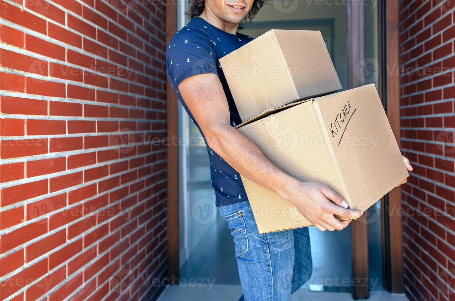 A man carrying two boxes in front of a brick wall photo