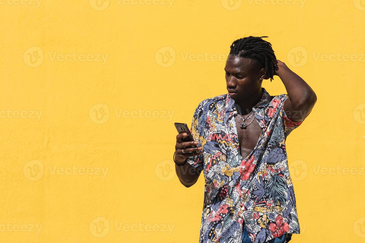 A man with dreadlocks standing in front of a yellow wall photo