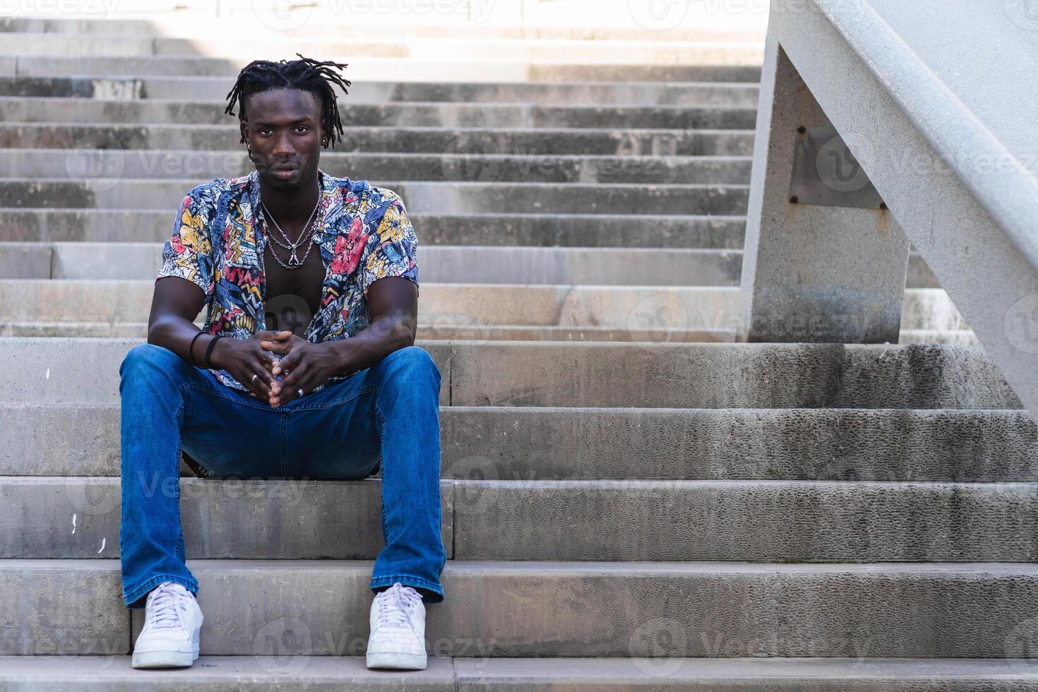A man sitting on some steps wearing blue jeans and a floral shirt photo