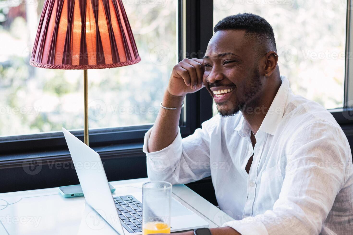 A smiling man sits at a table with a laptop photo