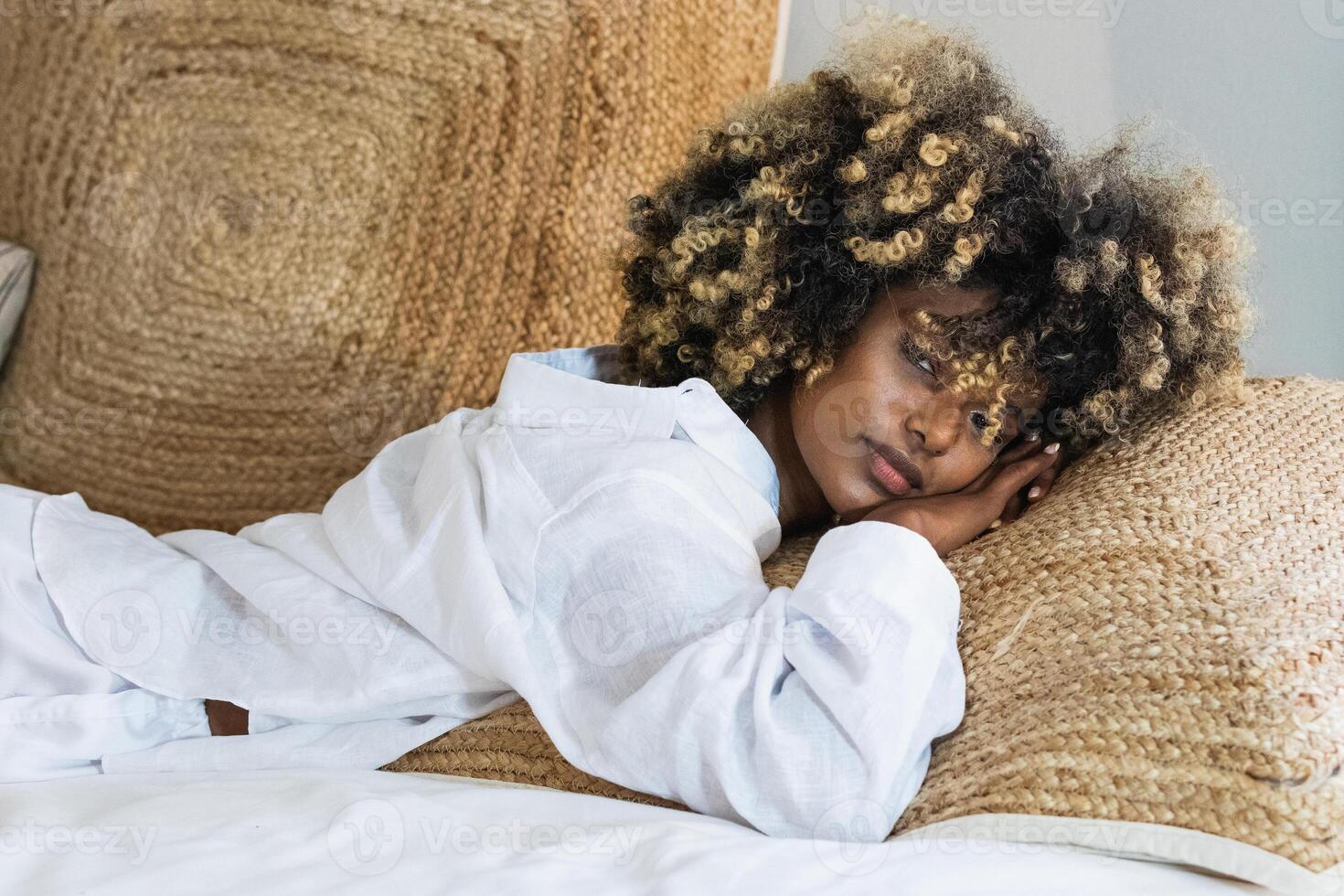 A woman with curly hair laying on a bed alone photo