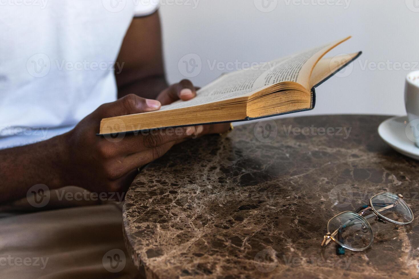 Man reading book on table with coffee and glasses photo